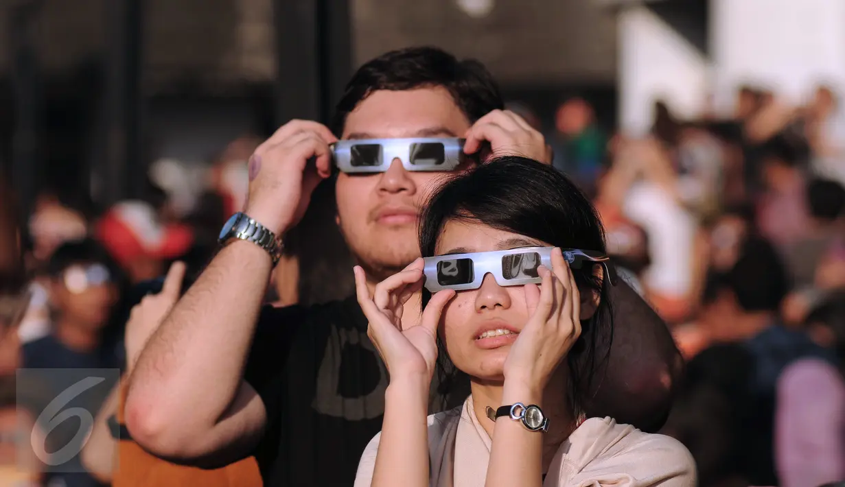 Sepasang muda mudi menggunakan kacamata khusus untuk melihat proses gerhana matahari di sekitar Taman Ismail Marzuki, Jakarta, Rabu (9/3/2016). Di Jakarta, fenomena gerhana matahari 90% bisa diamati selama 2,11 menit. (Liputan6.com/Helmi Fithriansyah)   