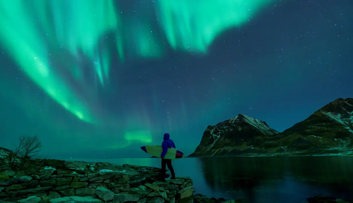 Seorang surfer membawa papannya melihat Cahaya Utara atau aurora borealis di Utakleiv, Norwegia utara (9/3). (AFP/Olivier Morin)