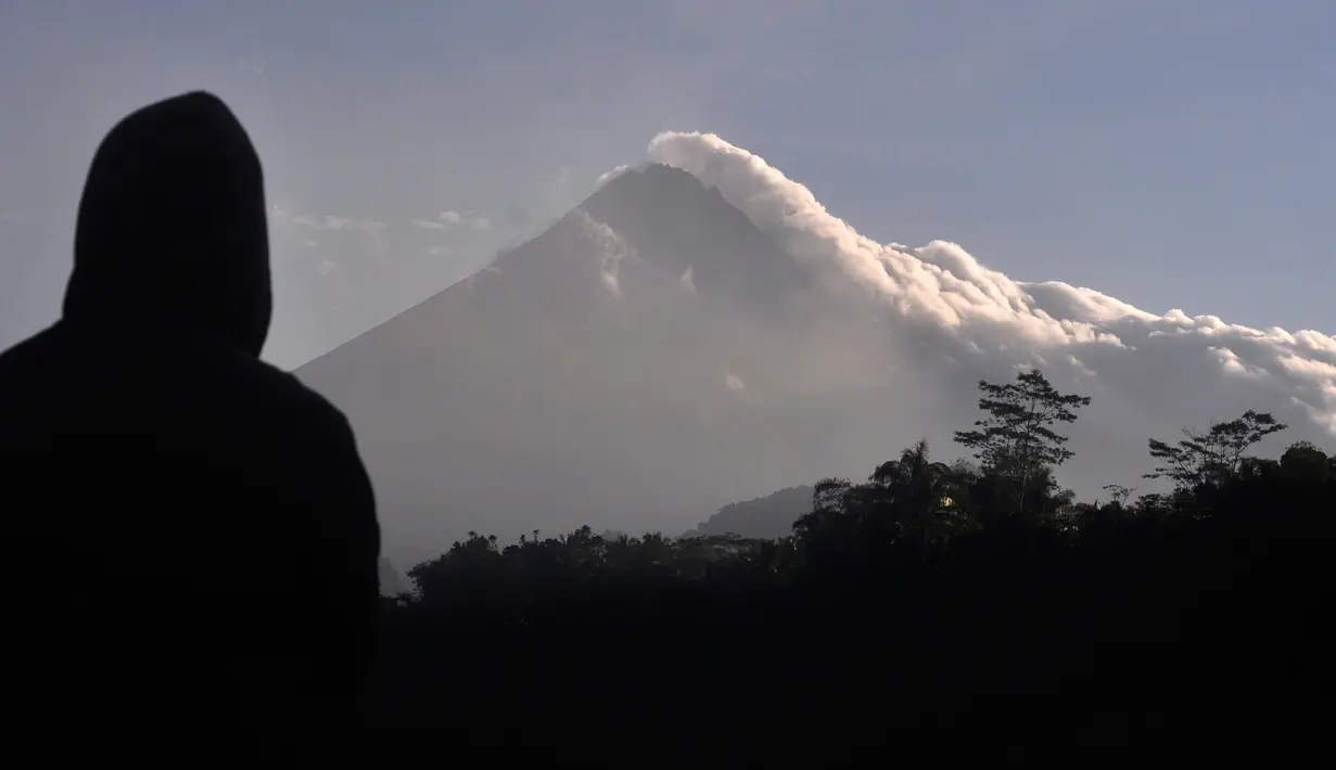 Seorang pria menyaksikan Gunung Merapi memuntahkan asap vulkanik di Yogyakarta, Indonesia, Selasa, (22/5). Pihak berwenang meningkatkan kewaspadaan terhadap Gunung Merapi yang bergejolak di pulau Jawa. (AP Photo/Slamet Riyadi)