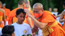 Foto yang diambil pada 17 Desember 2023 ini menunjukkan para biksu Buddha sedang mencukur rambut seorang samanera (calon biksu) muda. (DEVI RAHMAN/AFP)