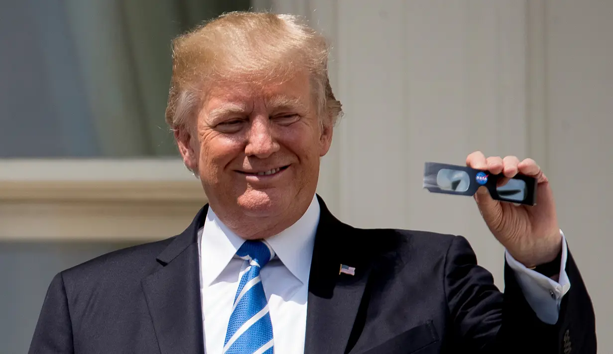 Presiden AS Donald Trump memperlihatkan kacamata pelindung sebelum menyaksikan  gerhana matahari dari balkon Gedung Putih di Washington, Senin (21/8). Gerhana matahari total di Amerika Serikat terlihat langsung di 14 negara bagian (AP Photo/Andrew Harnik)