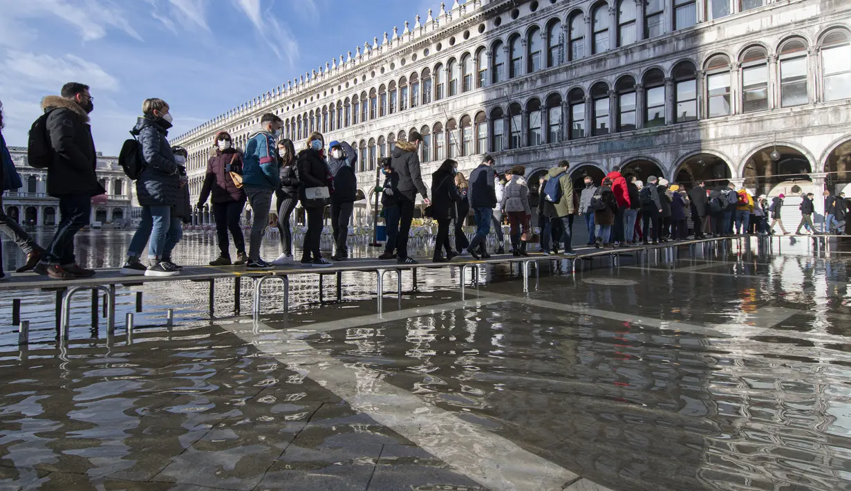 Orang menggunakan jembatan trestle untuk menyeberangi St Mark's Square yang dibanjiri air laut, di Venesia, Italia, Sabtu (4/12/2021). Air mencapai 99 sentimeter di atas permukaan laut dan bagian terendah kota tenggelam. (AP Photo/Luigi Costantini)