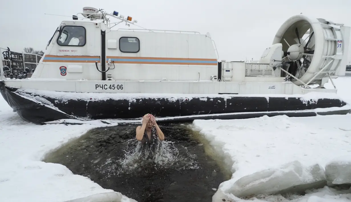 Petugas penyelamat yang duduk di perahu menyaksikan penganut Ortodoks Rusia terjun ke dalam air es selama perayaan Epiphany tradisional di St. Petersburg, Rusia (19/1/2021). Ritual ini untuk membersihkan diri dari segala dosa yang dilakukan selama setahun terakhir. (AP Photo/Dmitri Lovetsky)
