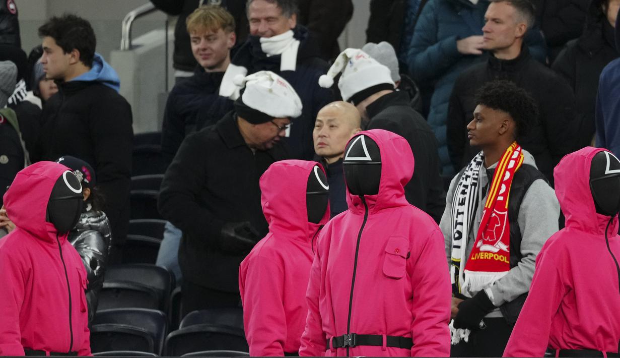 Orang-orang berpakaian seperti penjaga Squid Games dengan berdiri di area penonton selama pertandingan lanjutan Liga Inggris 2024/2025 antara Tottenham Hotspur melawan Liverpool di Stadion Tottenham Hotspur, London, Inggris Minggu (22/12/2024). Seperti diketahui, aksi tersebut ternyata merupakan promo musim kedua serial Korea Selatan tersebut. (AP Photo/Dave Shopland)