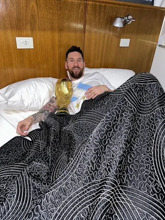 Kapten dan penyerang Argentina Lionel Messi berpose dengan Trofi Piala Dunia 2022 di tempat tidur di pusat pelatihan AFA di Ezeiza, Buenos Aires, Argentina pada 20 Desember 2022. Momen Messi ini viral di media sosial. Unggahan tersebut telah mengumpulkan lebih dari empat juta likes hanya dalam 15 menit. Hanya dalam waktu satu jam, foto Messi telah mencapai 19 juta likes. (Instagram/leomessi)