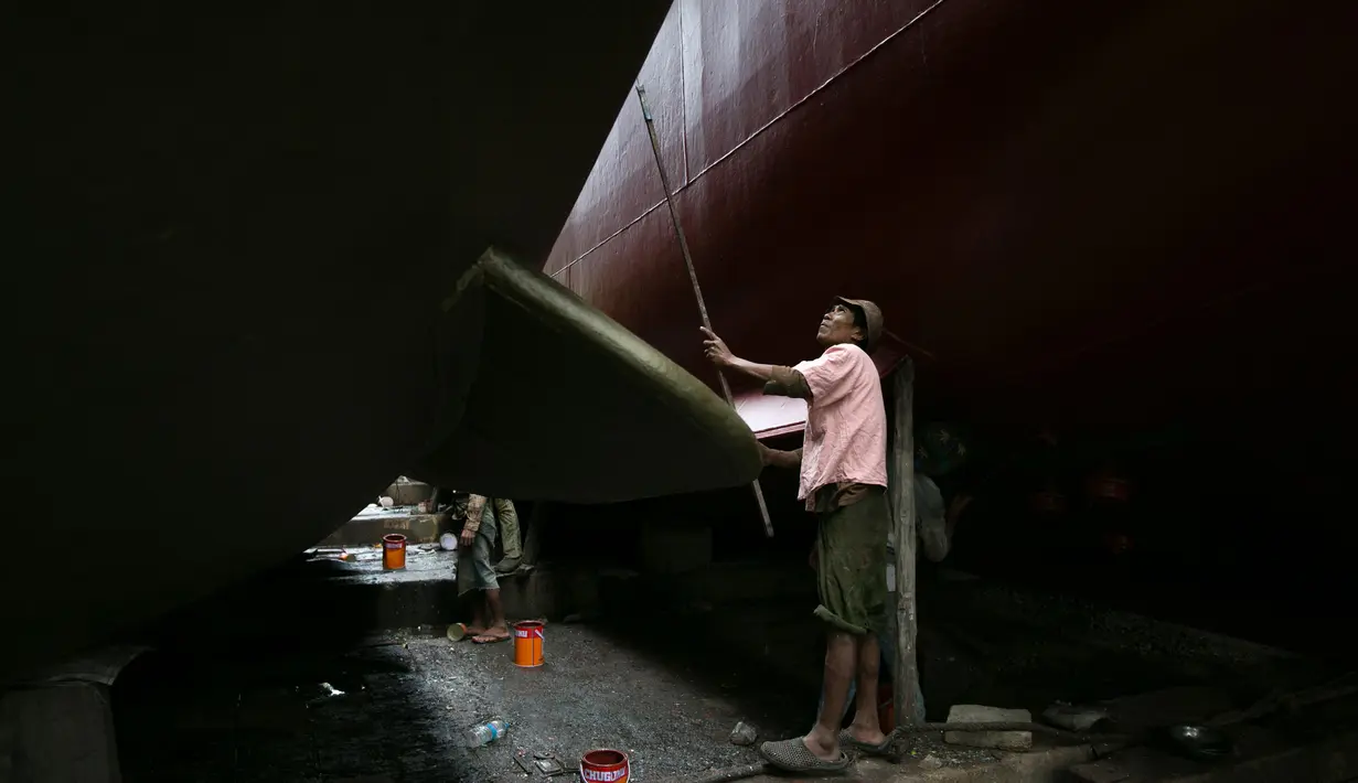 Seorang pekerja saat mengecat sebuah kapal di galangan kapal di tepi Sungai Yangon, yang terletak di pinggiran Yangon, Myanmar (30/7/2019). (AFP Phot/Sai Aung Main)