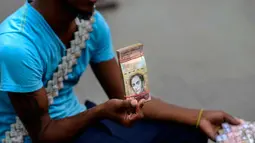Wilmer Rojas (25) menunjukkan lembaran mata uang Bolivar di Caracas, Venezuela, 30 Januari 2018. Dengan menggunakan jarum dan benang, Rojas menyulap lembaran Bolivar menjadi dompet hingga tas. (AFP Photo/Federico Parra)