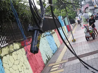 Pejalan kaki melintasi trotoar yang terhalang instalasi kabel di Jalan Kyai Maja, Jakarta, Rabu (10/4). Selain menganggu kenyamanan pejalan kaki, kondisi instalasi kabel yang semrawut tersebut juga berbahaya apabila mengandung aliran listrik. (Liputan6.com/Immanuel Antonius)