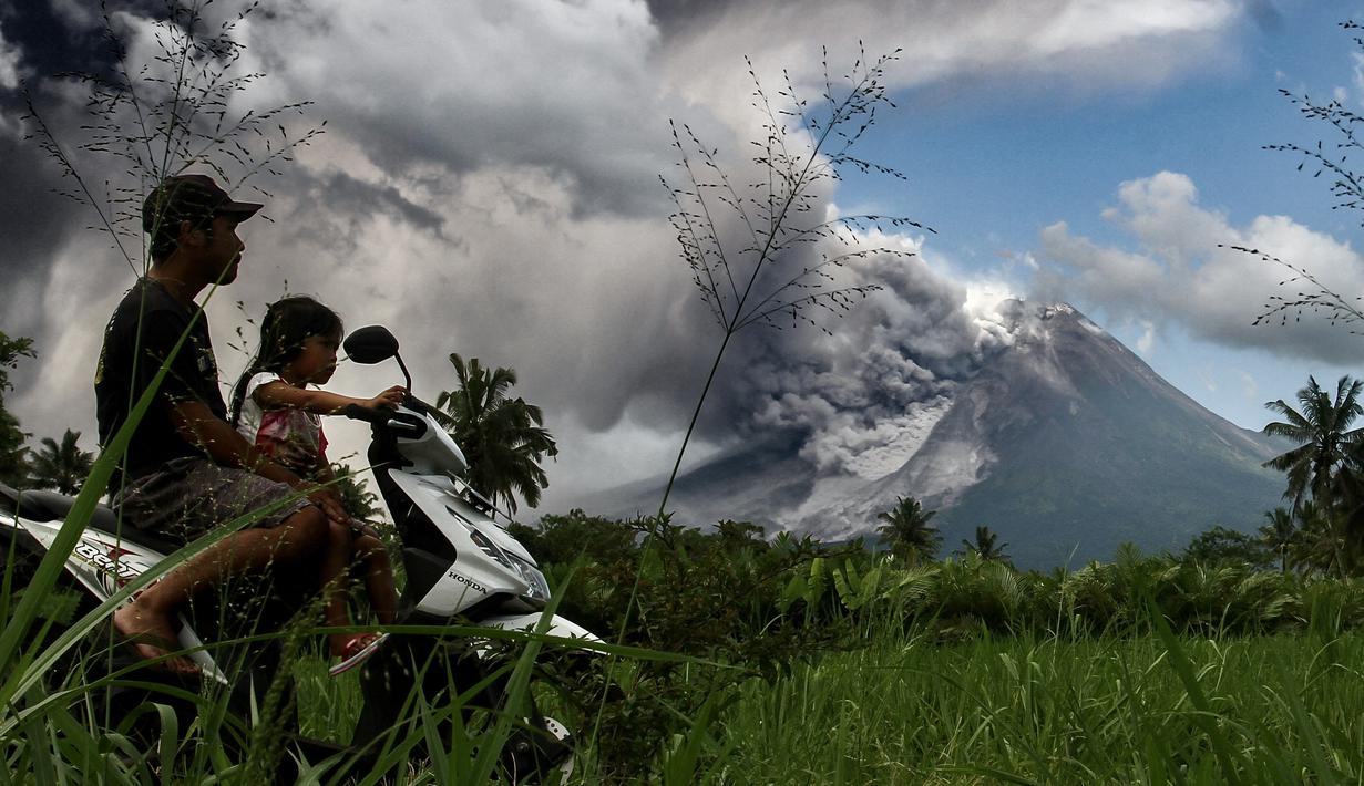 Pengendara motor melintas saat erupsi Gunung Merapi terlihat dari desa Tunggularum di Sleman pada 11 Maret 2023. Berdasarkan pengamatan pada Sabtu (11/3/2023) mulai pukul 06.00-12.00 WIB, BPPTKG mencatat satu kali guguran lava keluar dari Gunung Merapi dengan jarak luncur maksimal 1.500 meter ke arah barat daya. (AFP/Devi Rahman)