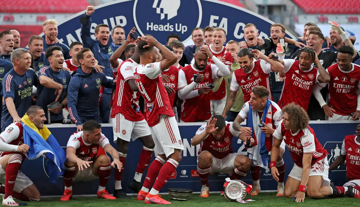 Striker Arsenal, Pierre-Emerick Aubameyang (tengah) menjatuhkan trofi saat merayakan gelar juara Piala FA usai mengalahkan Chelsea pada pertandingan final Piala FA di stadion Wembley, Minggu (2/8/2020).  Aubameyang terlihat kaget sambil memegang kepalanya saat trofi terjatuh. (Adam Davy/Pool via AP)