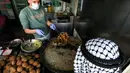 Juru masak Palestina mengenakan sarung tangan dan masker saat melayani pembeli falafel goreng di sebuah restoran lokal di kota Hebron, Tepi Barat yang diduduki pada 29 April  2020. Pada bulan suci Ramadan, falafel sering dimakan sebagai hidangan buka puasa. (HAZEM BADER / AFP)