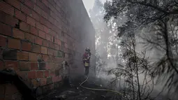 Seorang petugas pemadam kebakaran berdiri di sebelah sebuah rumah setelah kebakaran hebat di Sarnadas, Macao, di Portugal tengah (21/7/2019). Puluhan orang tewas akibat  kebakaran hutan tersebut. (AFP Photo/Patricia De Melo Moreira)