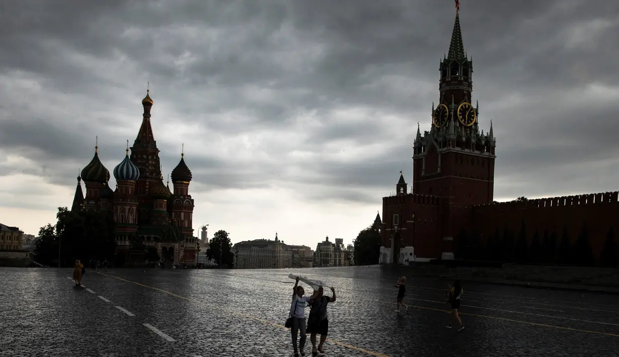 Orang-orang menutupi diri mereka dengan kantong plastik saat hujan di Lapangan Merah di Moskow, Rusia, 7 Juli 2020. Cuaca panas di Moskow terus berlanjut, dengan suhu diperkirakan mencapai lebih dari 30 derajat Celcius. (AP Photo/Pavel Golovkin)