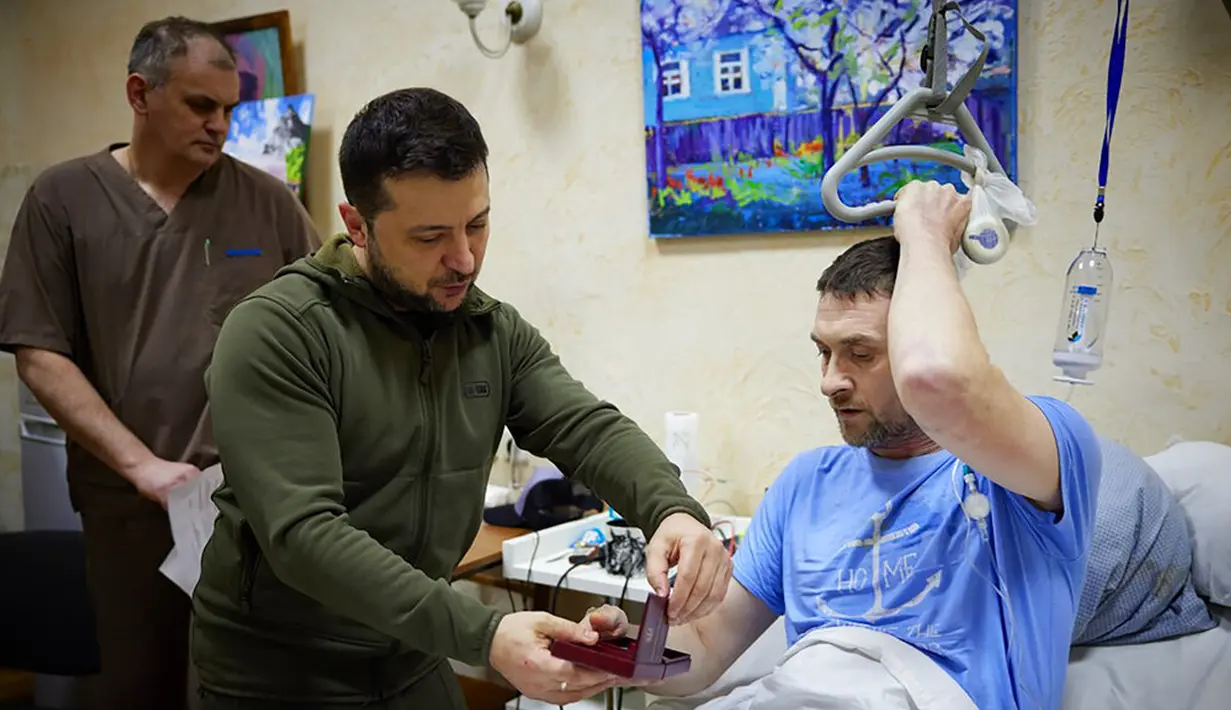 Dalam foto yang disediakan oleh Kantor Pers Kepresidenan Ukraina pada 13 Maret 2022, Presiden Ukraina Volodymyr Zelenskyy (tengah) menyerahkan medali negara kepada seorang tentara yang terluka saat kunjungannya ke sebuah rumah sakit di Kiev, Ukraina. (Ukrainian Presidential Press Office via AP)