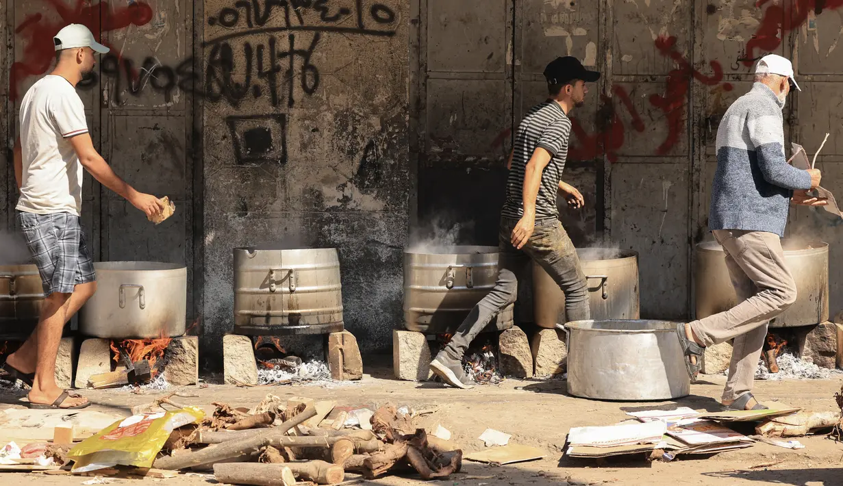 Orang-orang memasak dengan kayu bakar, di tengah kelangkaan bahan bakar dan gas, untuk menyediakan makanan bagi para pengungsi Palestina di tengah serangan Israel di Khan Yunis, di Jalur Gaza selatan pada 15 Oktober 2023. (MAHMUD HAMS / AFP)