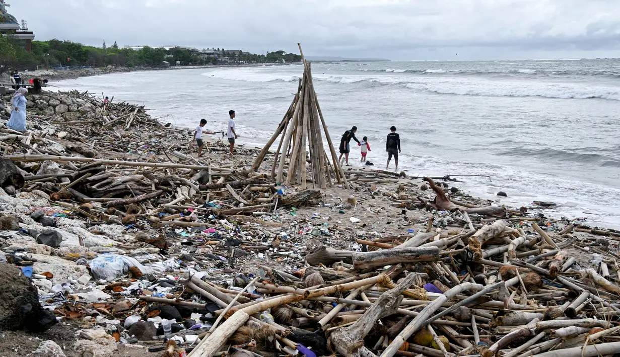 Orang-orang terlihat di samping tumpukan puing-puing dan sampah di di Pantai Kuta, Kabupaten Badung, Bali pada 26 Desember 2024. (SONNY TUMBELAKA/AFP)