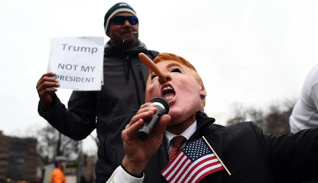 Aksi penolakan Donald Trump sebagai Presiden AS di Washington DC, Jumat (20/1). Seorang demonstran memakai topeng berwajah mirip Trump dengan hidung yang dipanjangkan. (AFP PHOTO / Jewel SAMAD)