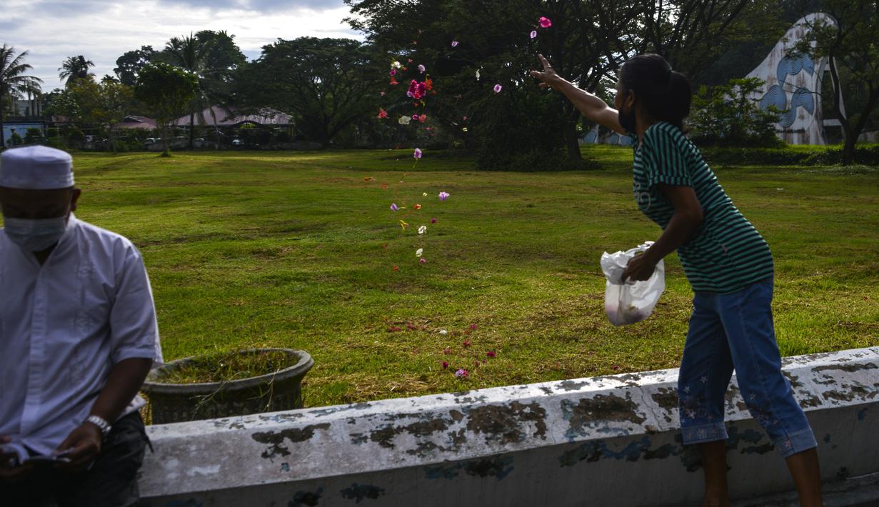 Seorang perempuan menaburkan kelopak bunga pada peringatan 16 tahun gempa bumi dan tsunami Aceh di sebuah kuburan massal di Siron, Sabtu (26/12/2020).  Peringatan di tengah pandemi COVID-19 itu tetap berlangsung secara sederhana melalui kegiatan ziarah kubur. (CHAIDEER MAHYUDDIN/AFP)