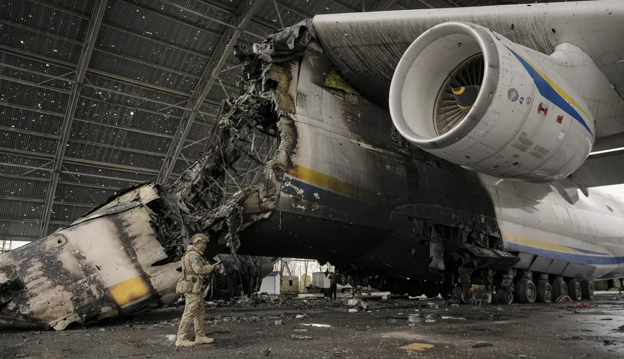 Prajurit Ukraina melewati pesawat Antonov An-225 Mriya yang hancur di bandara Antonov, Hostomel, 2 April 2022. Di pintu masuk Bandara Antonov, pasukan menjaga posisinya, tanda mereka memegang kendali penuh atas landasan pacu yang coba diserbu Rusia di hari-hari pertama perang (AP Photo/Vadim Ghirda)