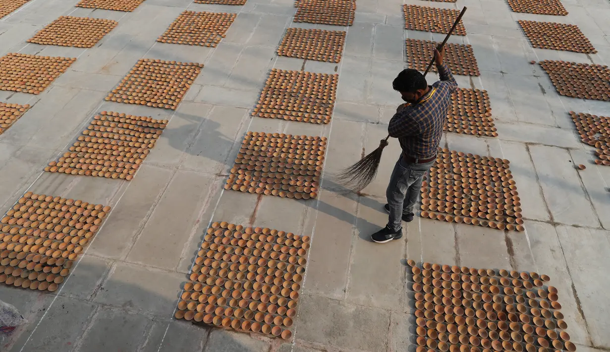 Seorang pria menyapu area di sekitar lampu tanah yang dipasang di tepi sungai Saryu di Ayodhya, India, Selasa (2/11/2021). Ratusan ribu lampu akan dinyalakan pada perayaan Deepotsav pada malam Diwali. (AP Photo/Rajesh Kumar Singh)