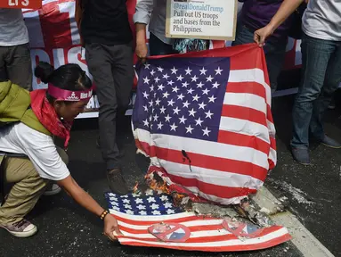 Aktivis membakar bendera AS dengan wajah Presiden terpilih Donald Trump di depan kedutaan AS, Manila, Filipina (20/1). Pengunjuk rasa menuding Presiden terpilih AS itu memiliki sifat seksisme, rasisme dan xenophobia. (AFP Photo/Ted Aljibe)