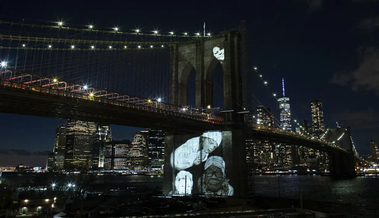 Gambar korban diproyeksikan pada Jembatan Brooklyn saat Hari Peringatan COVID-19 di Brooklyn, New York, Amerika Serikat, 14 Maret 2021. Acara diisi penyair muda, pertunjukan Hezekiah Walker, pendeta dari Gereja Tabernakel Love Fellowship serta Paduan Suara The Love Fellowship. (Kena Betancur/AFP)