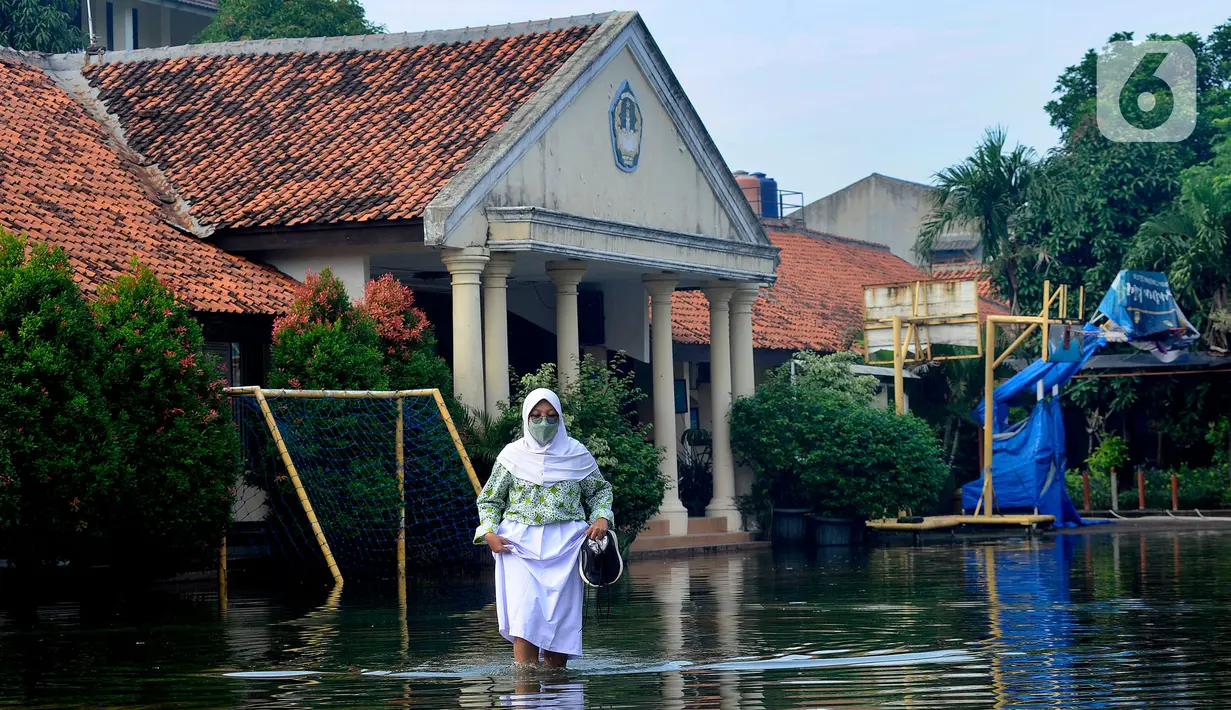Siswi berjalan melewati banjir yang menggenangi halaman  sekolah di SMAN 4 Tangsel, Pondok Ranji, Tangerang Selatan, Banten, Selasa (14/6/2022). Tiga  pekan lebih banjir merendam lapangan sekolah itu dikarenakan tertutupnya saluran air oleh sampah yang berasal dari tempat pembuangan sampah (TPS) ilegal. (merdeka.com/Arie Basuki)
