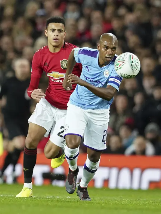 Gelandang Manchester City, Fernandinho berusaha membawa bola dari kawalan penyerang Manchester United, Mason Greenwood pada pertandingan leg pertama semifinal Piala Liga Inggris di Old Trafford (7/1/2020). City menang 3-1 atas MU. (AP Photo / Jon Super)