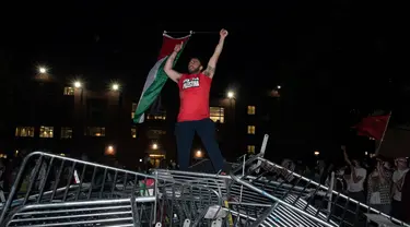 Seorang mahasiswa Universitas George Washington melambaikan bendera Palestina saat berdiri di atas barikade polisi yang diterobos untuk menduduki University Yard dalam aksi protes pro-Palestina di Washington, Minggu, 28 April 2024. (AP Photo/Cliff Owen)
