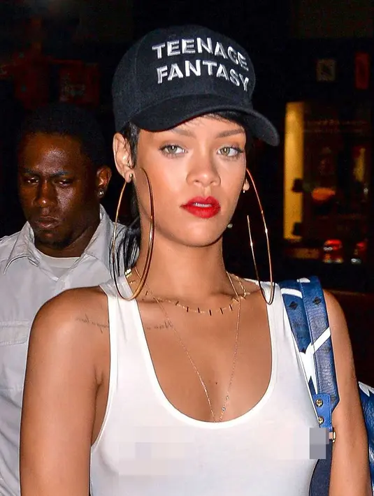 Dalam tank top putih, Rihanna tak menggunakan bra. Hal itu membuat tindikan di payudaranya terlihat. (REX/Shutterstock/HollywoodLife)