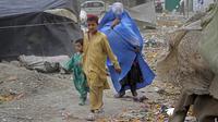 Seorang perempuan yang mengenakan burqa dan anak-anaknya berjalan di depan rumah mereka di Kabul, Afghanistan, 8 Mei 2022. Taliban memerintahkan perempuan Afghanistan untuk mengenakan pakaian dari kepala hingga ujung kaki atau burqa tradisional di depan umum. (AP Photo/Ebrahim Noroozi)