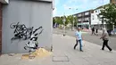 Pejalan kaki melewati stensil seorang anak menggali di pasir, yang menampilkan ciri-ciri seniman jalanan Banksy di dinding di Lowestoft di pantai timur Inggris pada 8 Agustus 2021. Karya tersebut belum diklaim oleh Banksy. (JUSTIN TALLIS / AFP)