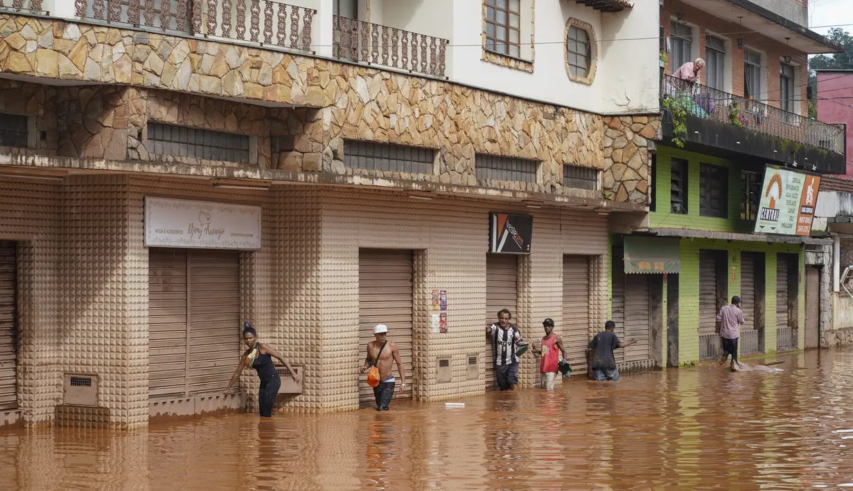 Orang-orang berjalan di jalan yang banjir di Raposos, negara bagian Minas Gerais, Brasil, Selasa (11/1/2022). Tanah longsor akibat hujan deras telah menewaskan sedikitnya 12 orang dan pihak berwenang sedang memantau bendungan yang bisa jebol. (AP Photo/Eugenio Savio)