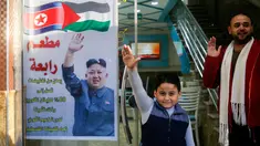 Salam Rabaa dan anaknya meniru pose pemimpin Korea Utara, Kim Jong-un pada poster di pintu restoran Rabaa di kamp pengungsi Jabalia, Gaza, Minggu (17/12). Restoran itu menawarkan potongan harga besar untuk pengunjung asal Korea Utara. (MOHAMMED ABED/AFP)