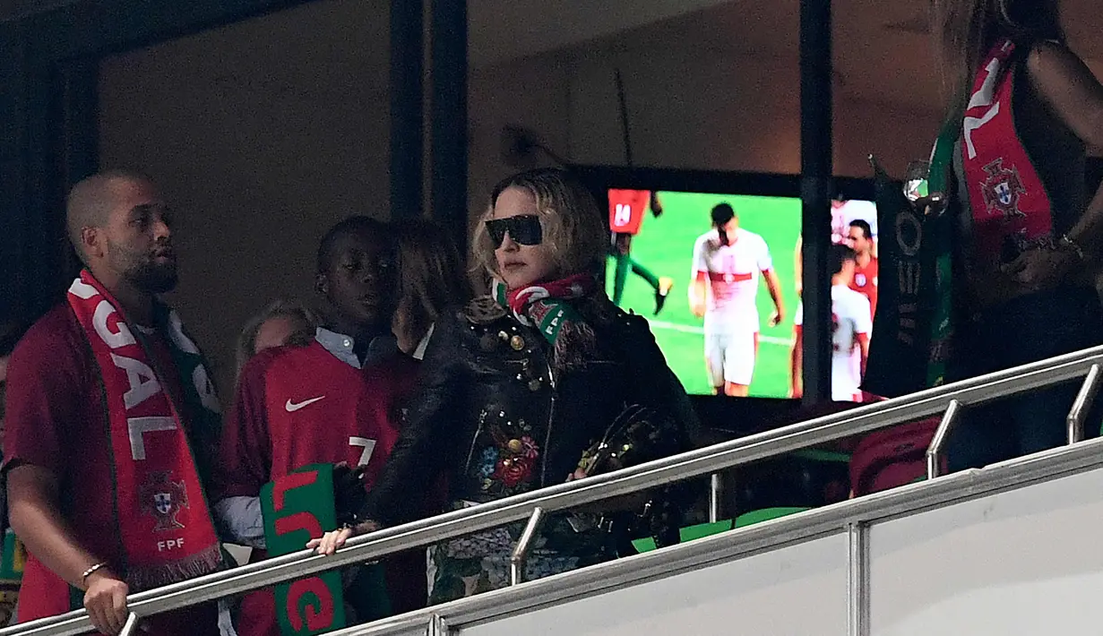 Penyanyi AS, Madonna (tengah) bersama anaknya David Banda menyaksikan pertandingan kualifikasi Piala Dunia 2018 antara Portugal dan Swiss di Stadion Luz di Lisbon (10/10). Madonna tampil mengenakan jaket dan kacamata hitam. (AFP Photo/Francisco Leong)