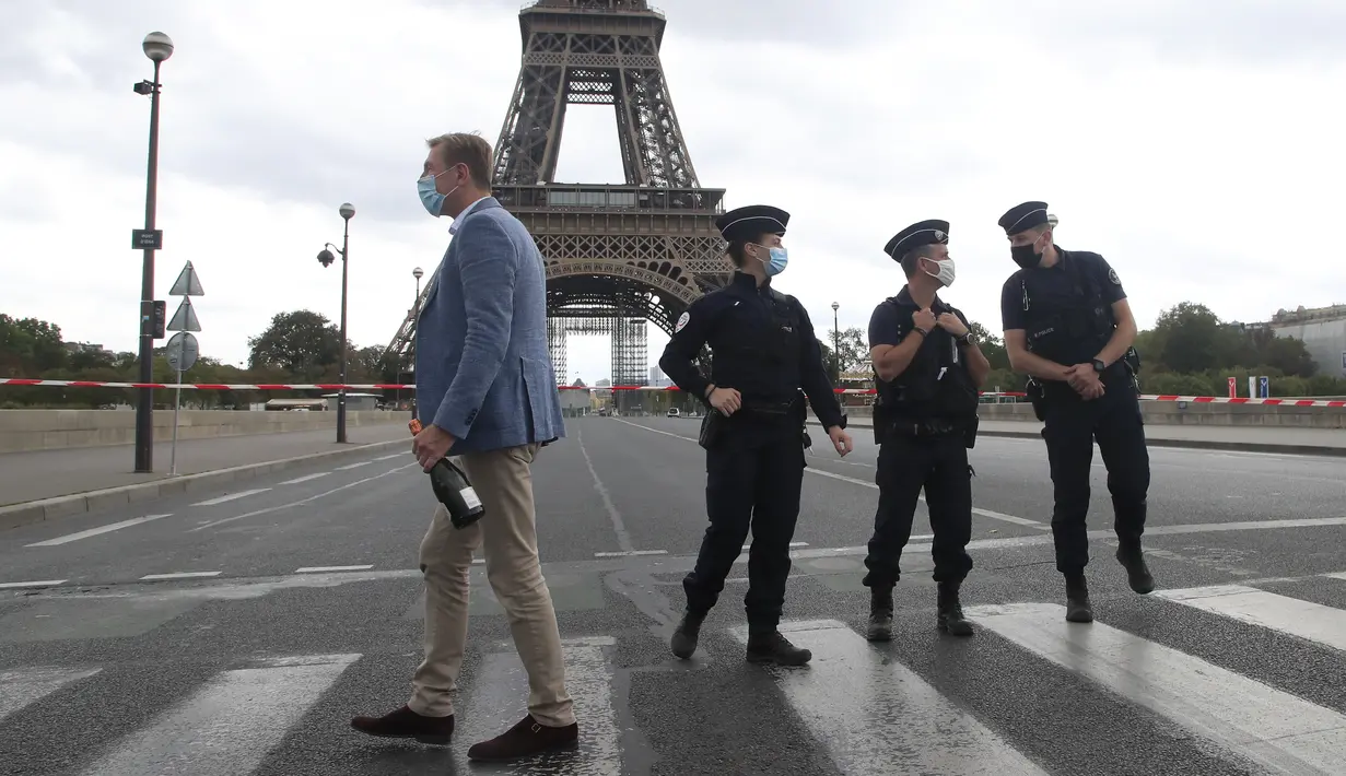 Seorang turis Rusia memegang sebotol sampanye berjalan melewati petugas polisi yang mengamankan jembatan menuju Menara Eiffel di Paris, Rabu (23/9/2020). Polisi Paris telah memblokir daerah sekitar Menara Eiffel setelah ancaman bom telepon. (AP Photo / Michel Euler)