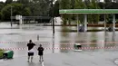 Sebuah keluarga berjalan mengunjungi pompa bensin yang terendam banjir di pinggiran barat daya Camden, Sydney, Australia, Selasa (8/3/2022). (Muhammad FAROOQ/AFP)