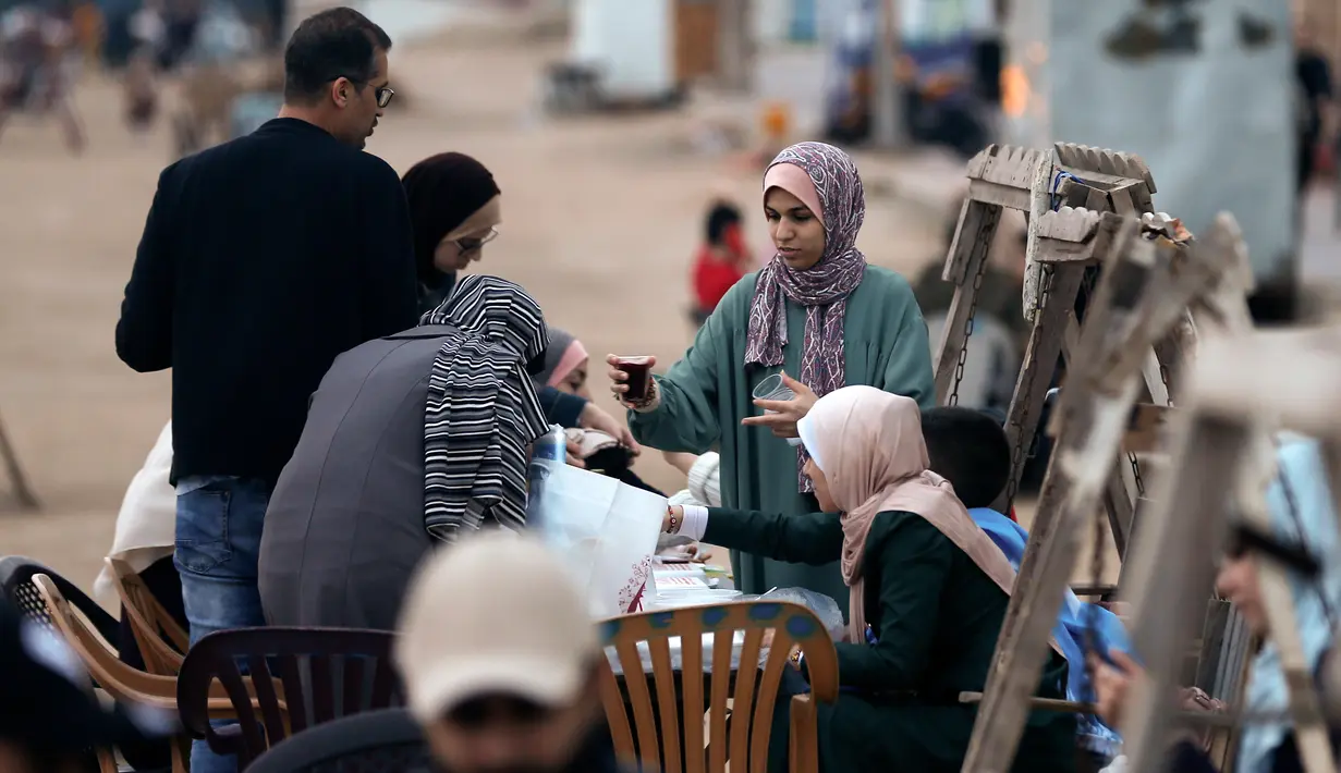 Warga Palestina berkumpul untuk berbagi makanan buka puasa selama bulan suci Ramadan, saat pandemi virus corona, di sepanjang pantai kota Gaza pada 13 Mei 2020. Mereka menunggu waktu berbuka puasa sambil menyaksikan matahari terbenam. (Photo by MAHMUD HAMS / AFP)