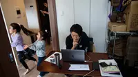 Gambar pada 23 Maret 2020 menunjukkan seorang karyawan di sebuah perusahaan startup, Yuki Sato, bekerja dari rumah selama pandemi virus corona Covid-19  saat dua putrinya, Yurina dan Hinano bermain dan sang istri menggunakan ponsel di Tokyo. (Behrouz MEHRI / AFP)