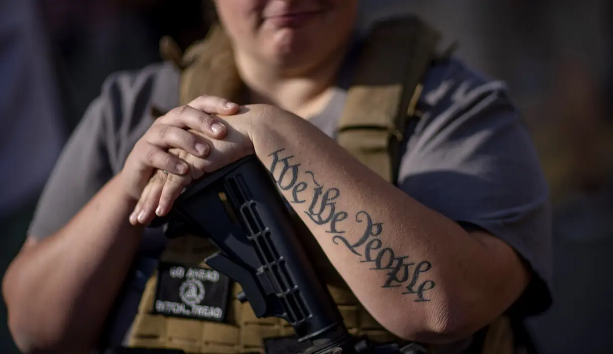 Tato "We The People", frasa dari Konstitusi Amerika Serikat, menghiasi lengan pendukung Donald Trump, Michelle Gregoire, saat meletakkan tangannya di atas senjatanya selama protes atas hasil pemilu di luar papan penghitungan pusat di TFC Center, Detroit , Jumat (6/11/2020). (AP Photo/David Goldman)