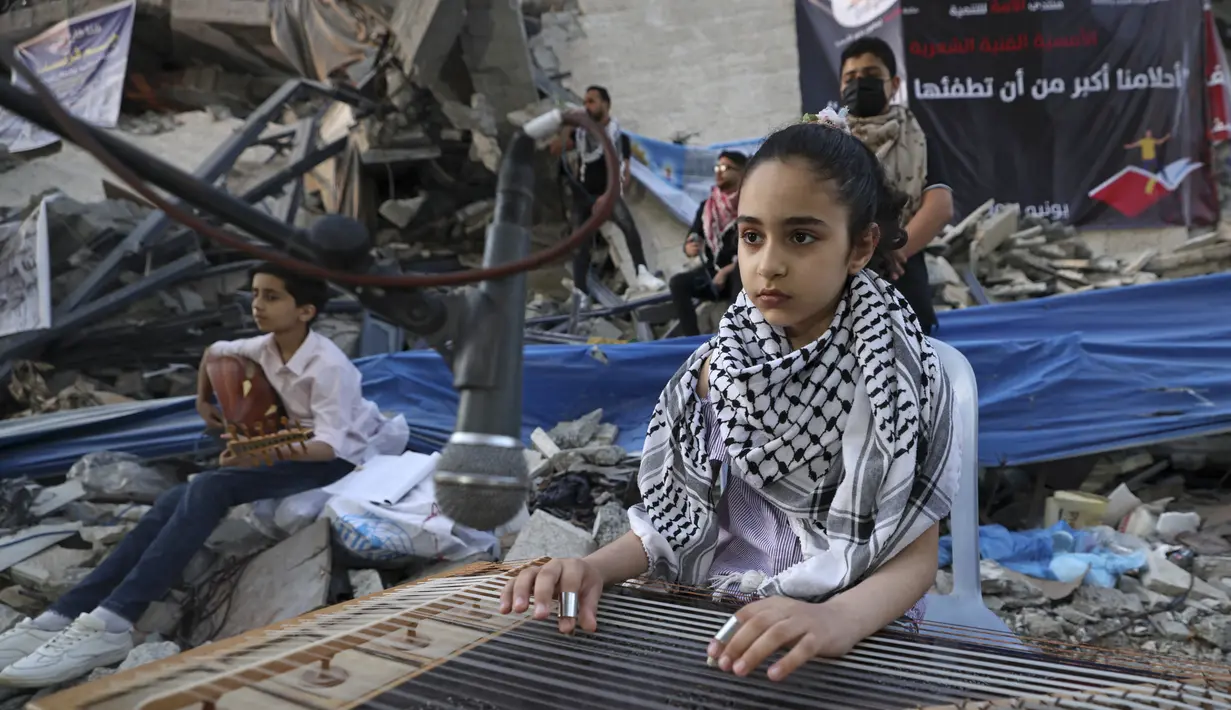 Seorang gadis Palestina memainkan alat musik saat tampil di puing-puing Menara Hanadi di Kota Gaza (2/6/2021). Acara diselenggarakan oleh Komite Pemuda dan Kebudayaan Palestina lebih dari seminggu setelah gencatan senjata mengakhiri 11 hari permusuhan antara Israel dan Hamas. (AFP Photo/Mohammed Abe