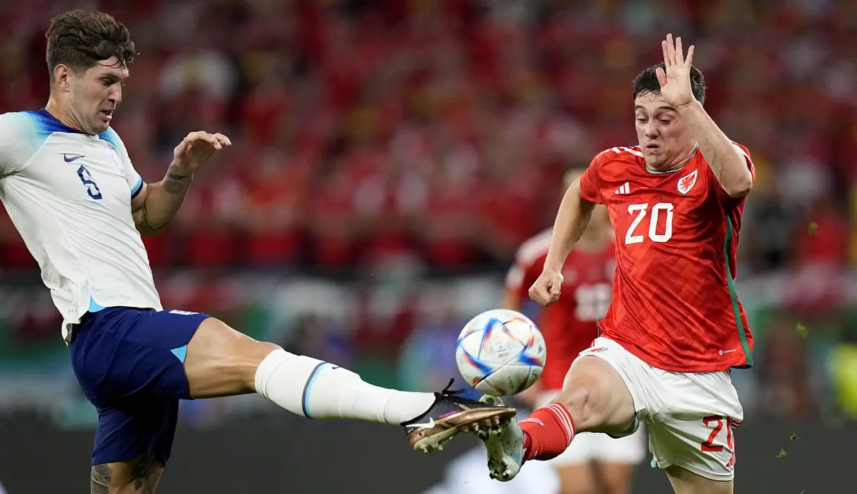 Bek Inggris John Stones berebut bola dengan penyerang Wales Daniel James pada pertandingan terakhir Grup B di Ahmad bin Ali Stadium, Rabu (30/11/2022) dini hari WIB. Inggris bertemu runner-up Grup A Senegal akhir pekan nanti. (AP Photo/Pavel Golovkin)