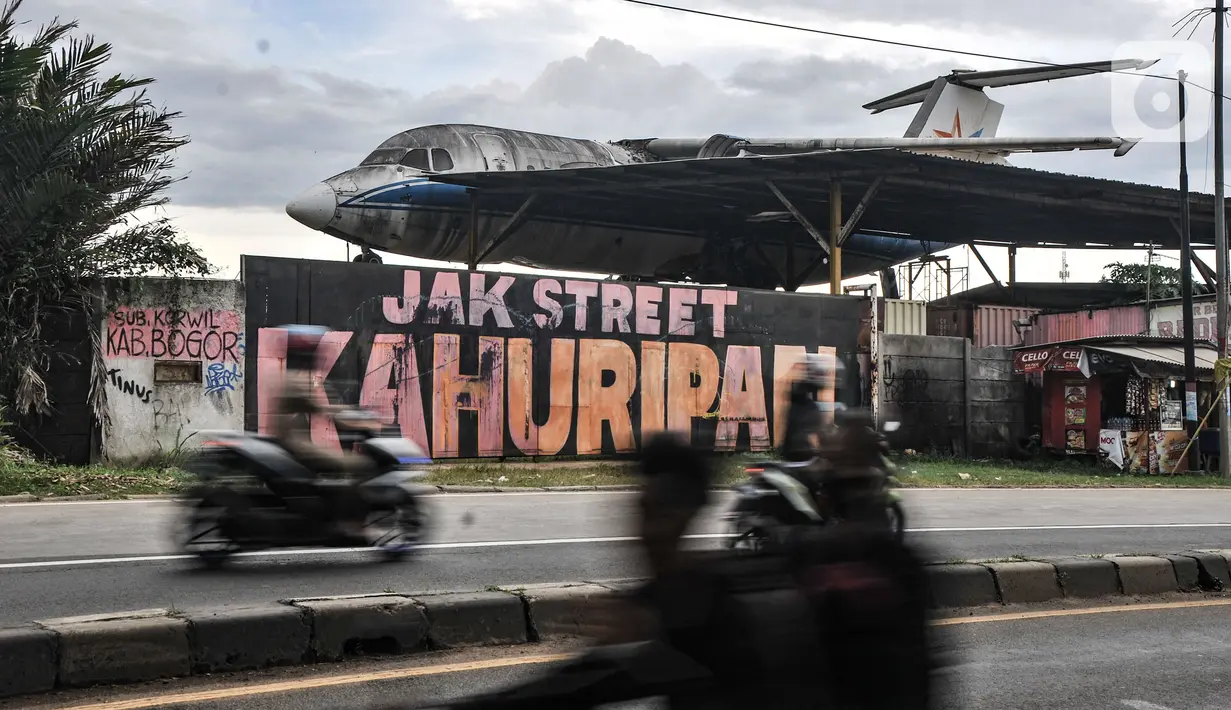 Pengendara motor melintasi depan gudang penyimpangan pesawat di Desa Pondok Udik, Bogor, Minggu (9/1/2022). Kepala Desa Pondok Udik, Entis Sutisna mengungkapkan bangkai pesawat komersil tersebut telah ada sejak 2019 dan akan diubah menjadi restoran oleh sang pemilik. (merdeka.com/Iqbal S Nugroho)