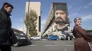 Warga setempat berjalan di depan mural legenda sepak bola, Diego Armando Maradona di San Giovanni a Teduccio, Italia (28/2). Mural tersebut digambar di sebuah bangunan pemukiman warga di distrik yang dikenal dengan Bronx. (AFP/Renato Esposito)