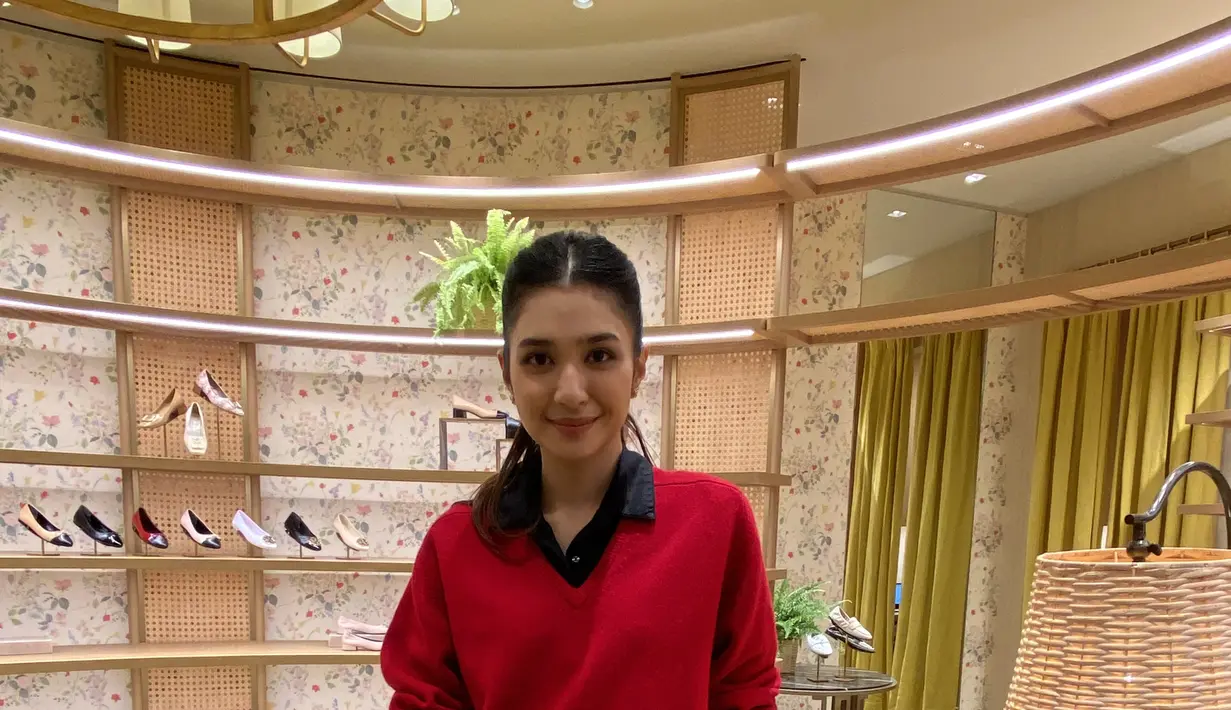 Mikha Tambayong tampil smart casual mengenakan inner kemeja hitam dipadukan v neck sweater merah serta celana coklat.  [Anisha Saktian]
