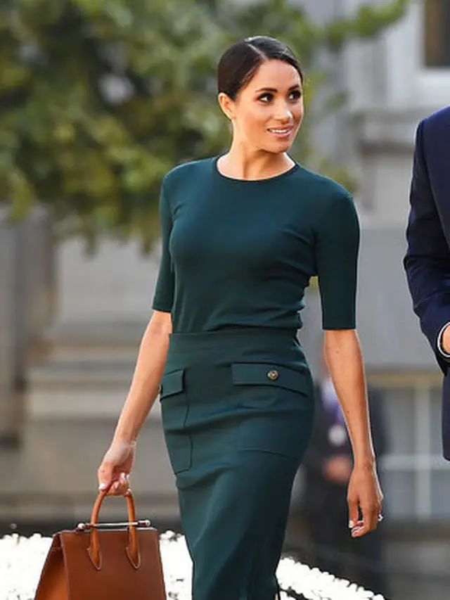 Meghan mengenakan tas tangan berwarna coklat brand Strathberry.