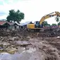 Warga menyaksikan ekskavator membersihkan puing pada daerah yang terkena banjir bandang di Waiwerang, Pulau Adonara, Nusa Tenggara Timur, Selasa (6/4/2021). Tim penyelamat terus menggali puing tanah longsor untuk mencari korban yang terkubur usai bencana banjir bandang. (AP Photo/Rofinus Monteiro)