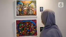Pengunjung menyaksikan karya lukis yang bertajuk 'Membangun Harmoni' di Museum Basoeki Abdullah, Jakarta, Sabtu (18/12/2021). Pameran tersebut dibisa disaksikan dari 19 Desember 2021 hingga Januari 2022. (Liputan6.com/Herman Zakharia)
