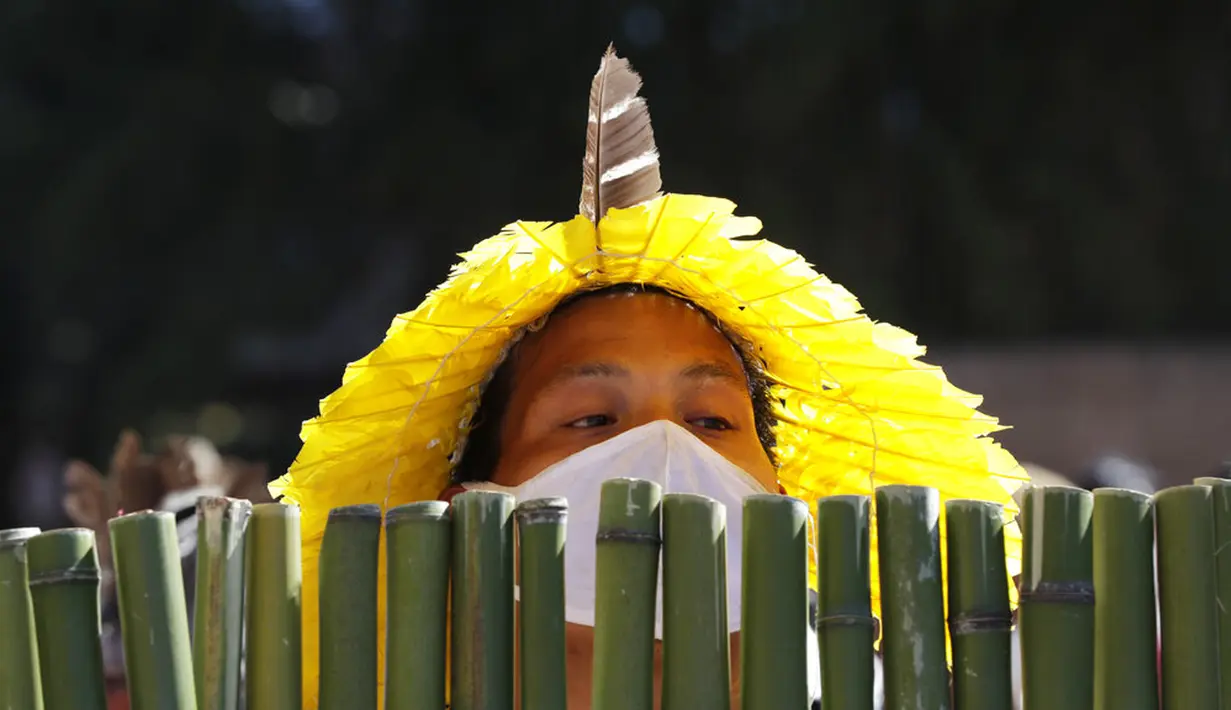 Seorang penduduk asli Brasil mengintip dari balik perisai bambu saat demo menentang RUU Reformasi Agraria di luar Kongres di Brasilia, Brasil, Selasa (22/6/2021). Penduduk asli Brasil menilai RUU Reformasi Agraria akan membatasi pengakuan lahan reservasi. (AP Photo/Eraldo Peres)