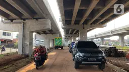 Pedagang melintasi mobil yang parkir di kolong jalan tol Becakayu di kawasan Cipinang Muara, Jakarta, Jumat (13/3/2020). Minimnya lahan parkir membuat sebagian orang tetap memarkirkan kendaraannya di kolong tol tersebut, meskipun telah terpampang larangan parkir. (Liputan6.com/Immanuel Antonius)